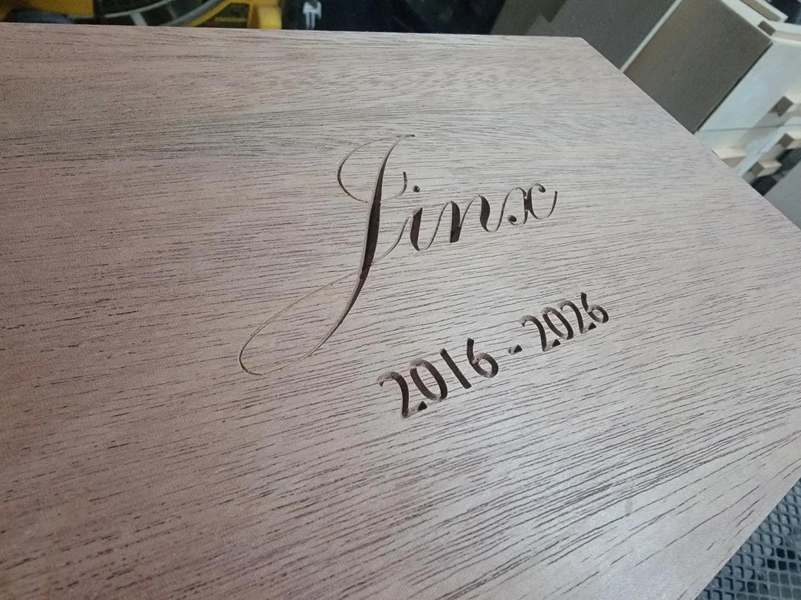 A mahogany box lid with Jinx carved in flowing script and 2016 - 2026 carved below it.
